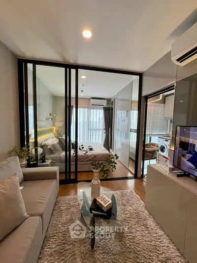 Modern living room with glass partition leading to a stylish bedroom, featuring elegant decor and natural light.