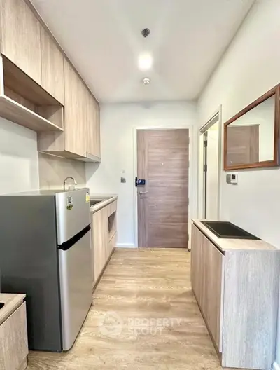 Modern kitchen with sleek wooden cabinets and stainless steel fridge in compact apartment.