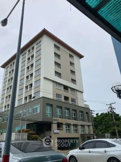 Modern multi-story residential building with parking area and street view.