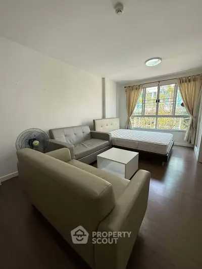 Spacious studio apartment with cozy seating and large window view.