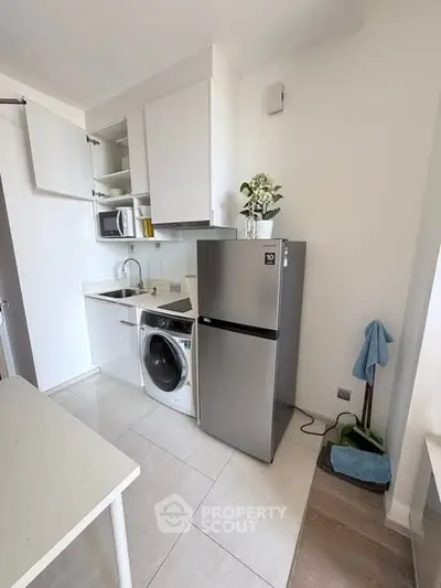 Modern compact kitchen with stainless steel fridge and washing machine, featuring sleek white cabinetry and tile flooring.