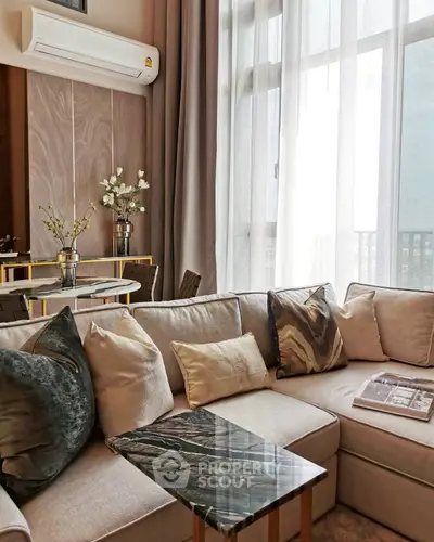 Elegant living room with plush sofa, marble table, and natural light through sheer curtains.