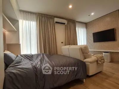 Modern bedroom with cozy bed, stylish armchair, and wall-mounted TV in a well-lit space.