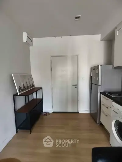 Modern kitchen with sleek appliances and wooden flooring, featuring a washing machine and fridge.
