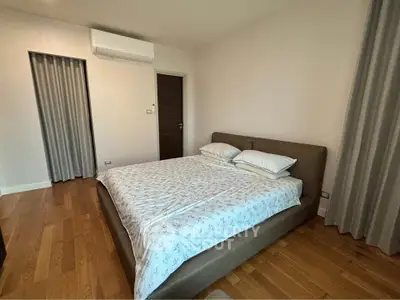 Spacious bedroom with modern decor and wooden flooring, featuring a comfortable bed and air conditioning.