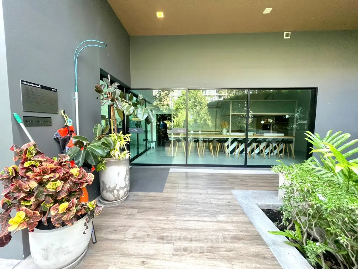 Modern building entrance with glass walls and lush greenery, showcasing a stylish and inviting atmosphere.