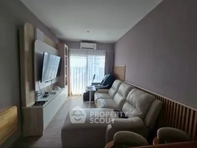 Modern living room with sleek furniture and large TV, featuring natural light from a window.