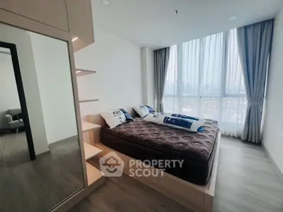 Modern bedroom with large window and stylish decor in high-rise apartment.