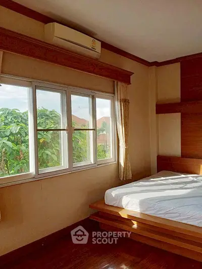 Cozy bedroom with large window and natural light, featuring wooden accents and air conditioning.