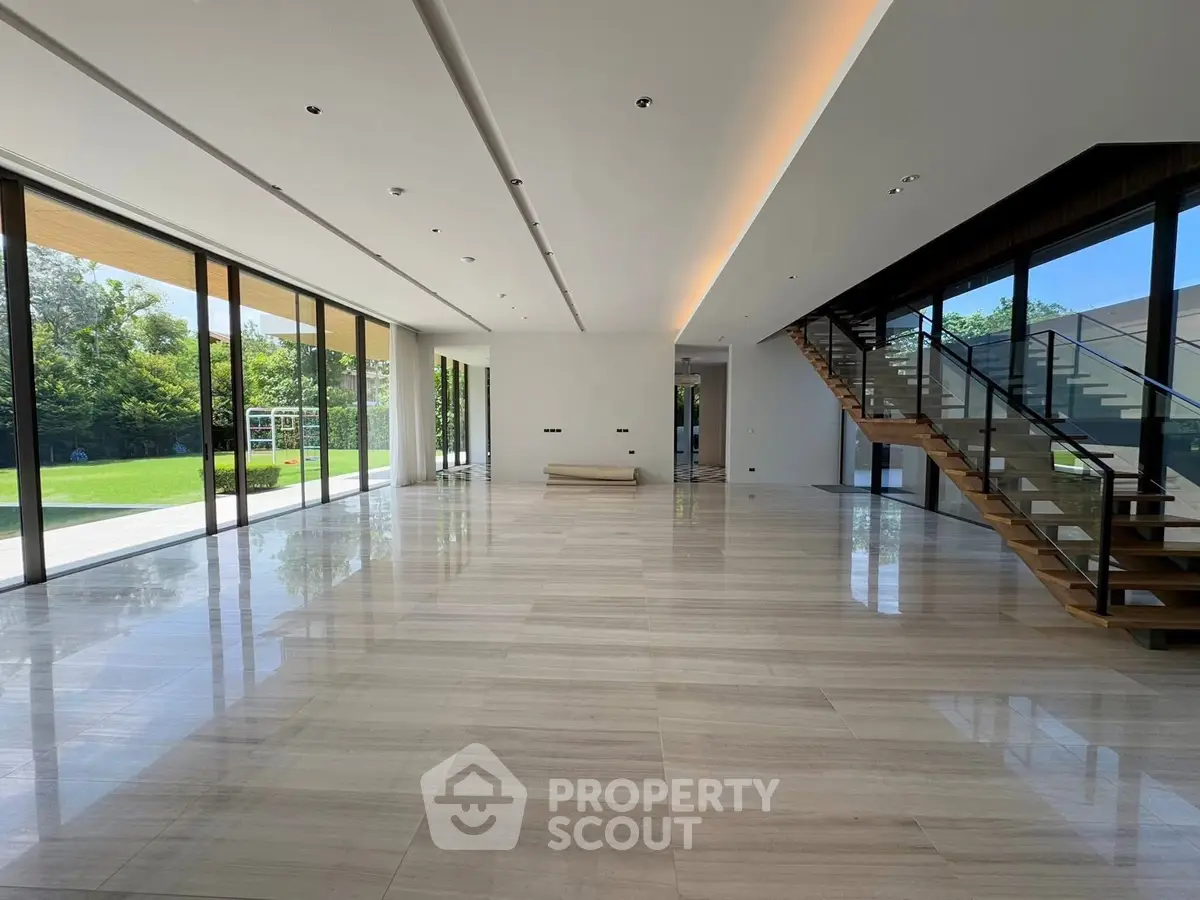 Spacious modern living room with floor-to-ceiling windows and elegant staircase.