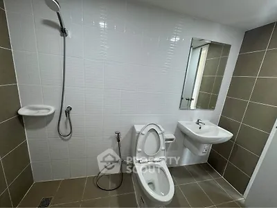 Modern bathroom with sleek fixtures and neutral tiles, featuring a shower and toilet.