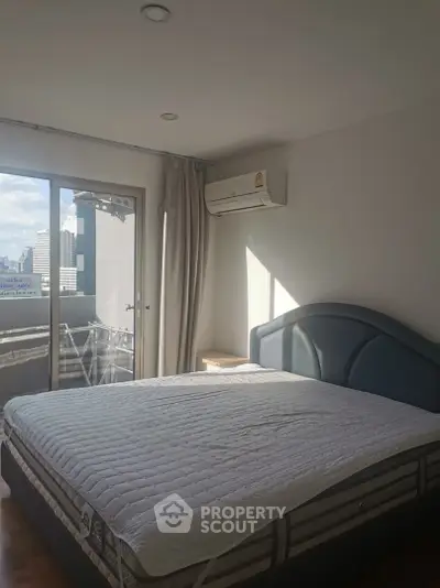 Spacious bedroom with city view and natural light, featuring a comfortable bed and air conditioning.
