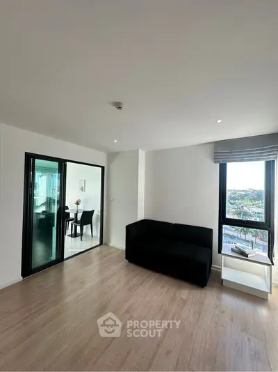 Modern living room with sleek black sofa and large window offering city views, adjacent to dining area.