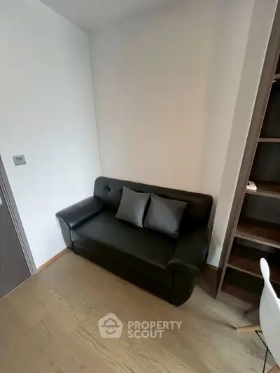 Cozy small living room with black leather sofa and modern shelving unit.