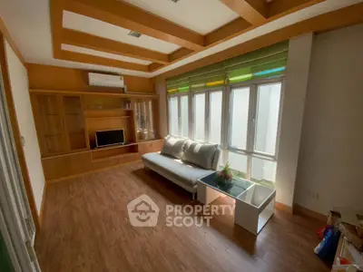 Spacious living room with wooden flooring and modern furniture, featuring large windows for natural light.