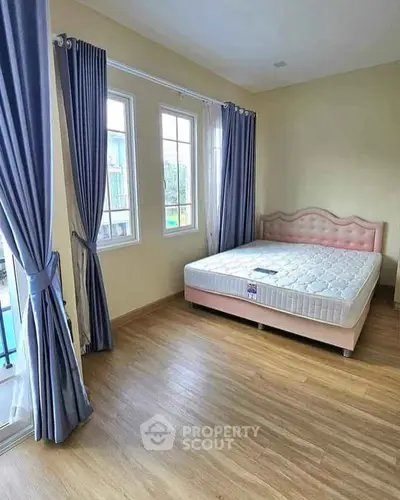 Spacious bedroom with large windows and elegant curtains, featuring a comfortable bed.