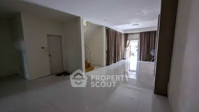 Spacious modern living room with large windows and elegant curtains, featuring a staircase and glossy tiled floor.