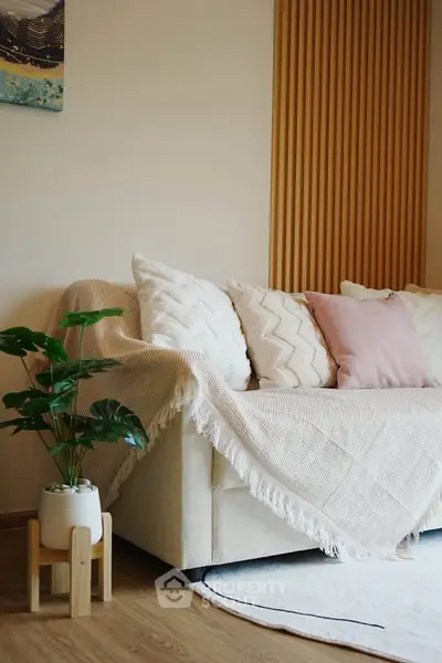 Cozy living room with stylish beige sofa and decorative pillows, wooden accents, and indoor plant.