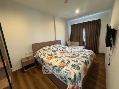 Cozy bedroom with floral bedding and modern decor, featuring a wall-mounted TV and wooden flooring.