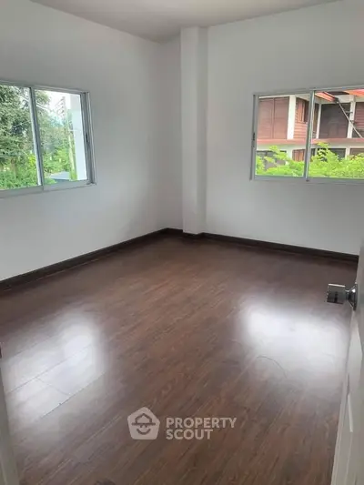 Spacious empty room with wooden flooring and large windows offering natural light.