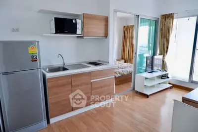 Modern studio apartment with compact kitchen and cozy living area, featuring wooden flooring and natural light.