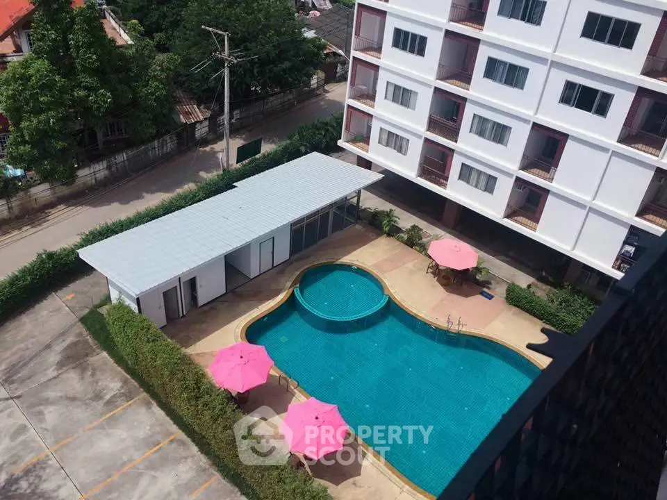 Stunning aerial view of modern apartment building with inviting pool and vibrant pink umbrellas.