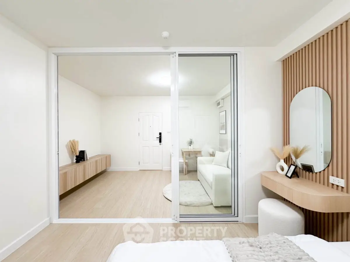 Modern bedroom with sliding glass doors leading to a stylish living room, featuring minimalist decor and neutral tones.