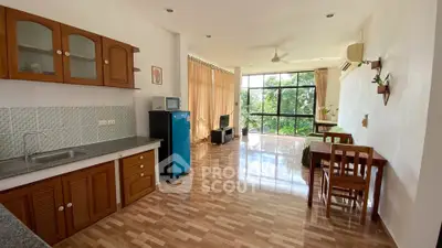Spacious open-plan living area with kitchen and large windows offering a lush green view.