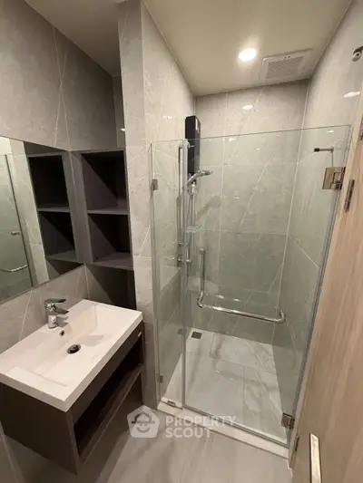 Modern bathroom with glass shower and sleek vanity in contemporary apartment.