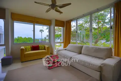 Bright living room with large windows and cozy seating, offering a serene garden view.