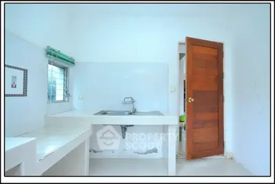 Minimalist kitchen with white tiles and wooden door, featuring a sleek sink and ample counter space.