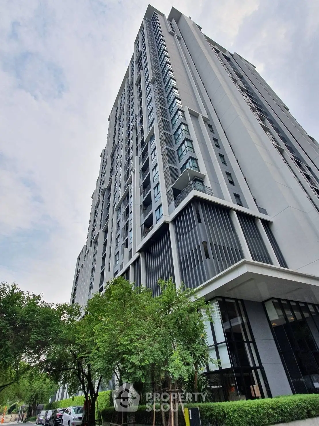 Modern high-rise building with sleek design and lush greenery at the base, showcasing urban living.