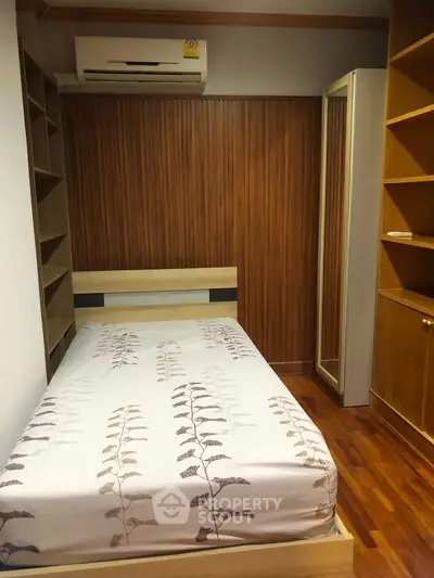 Cozy bedroom with wooden flooring and built-in shelves, featuring a single bed and air conditioning.