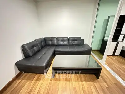 Modern living room with sleek black leather sectional sofa and glass coffee table on wooden flooring.