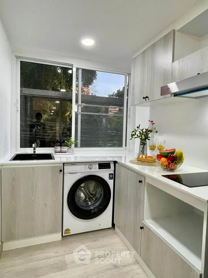 Modern kitchen with sleek cabinetry, washing machine, and large window offering natural light.