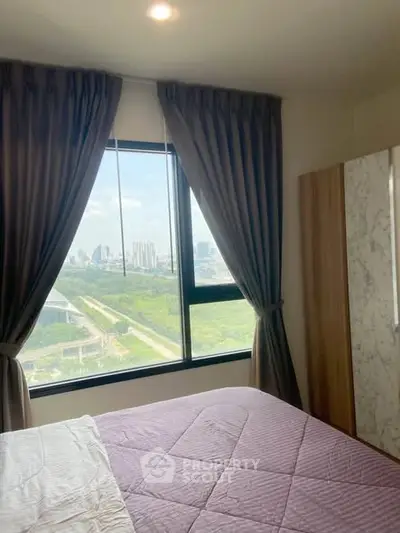 Cozy bedroom with large window offering stunning city and greenery views, perfect for relaxation.