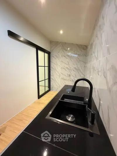 Modern kitchen with sleek black countertop and marble walls, featuring a stylish black faucet and sliding glass door.