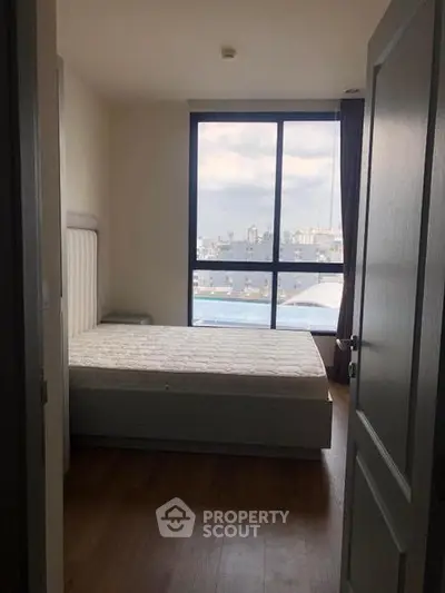 Cozy bedroom with large window offering city views, featuring a comfortable bed and wooden flooring.