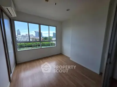 Bright empty room with large windows offering stunning city views and wooden flooring.