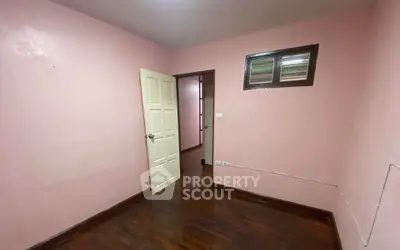 Cozy pink-walled room with wooden flooring and open door, perfect for a small bedroom or study.