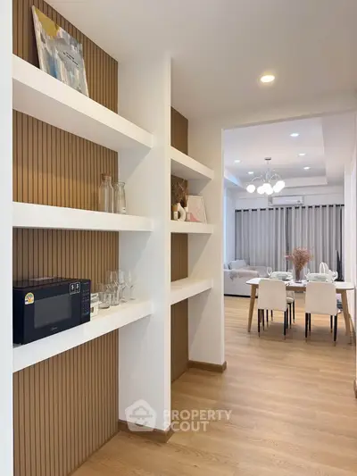 Modern open-plan living and dining area with stylish shelving and wooden flooring.