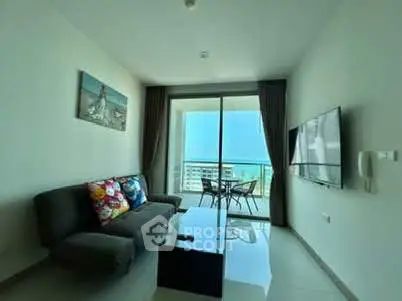 Modern living room with ocean view and balcony access, featuring sleek furniture and large TV.