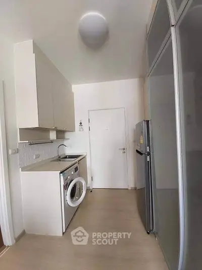 Modern kitchen with sleek appliances and ample storage space, featuring a washing machine and refrigerator.