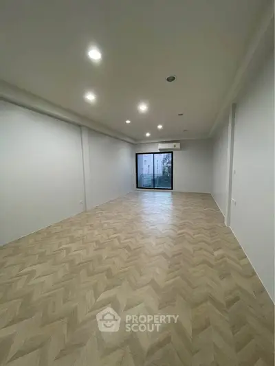 Spacious empty room with elegant herringbone flooring and recessed lighting, perfect for customization.