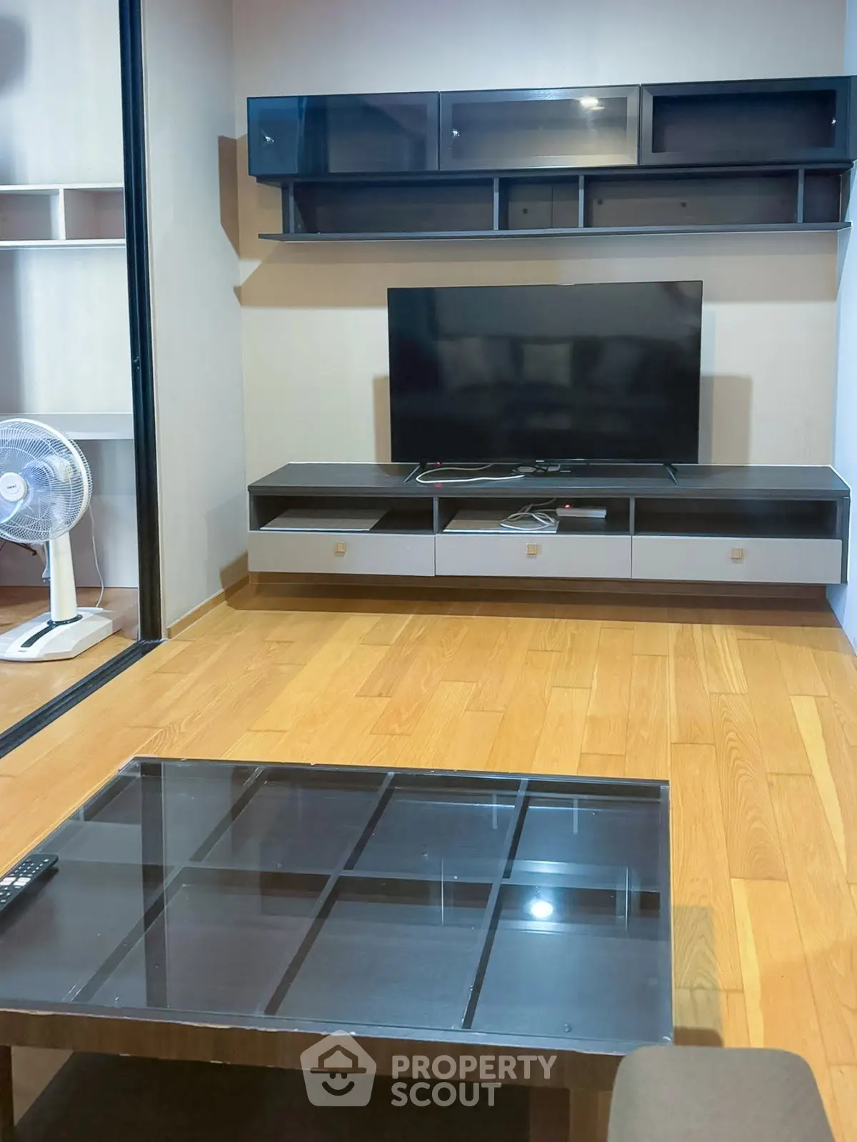 Modern living room with sleek TV stand and glass coffee table on wooden flooring.