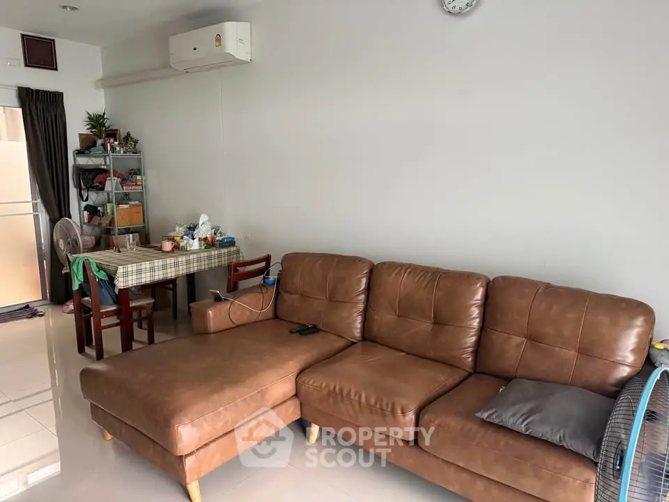 Spacious living room with brown leather sofa and dining area, featuring modern decor and air conditioning.