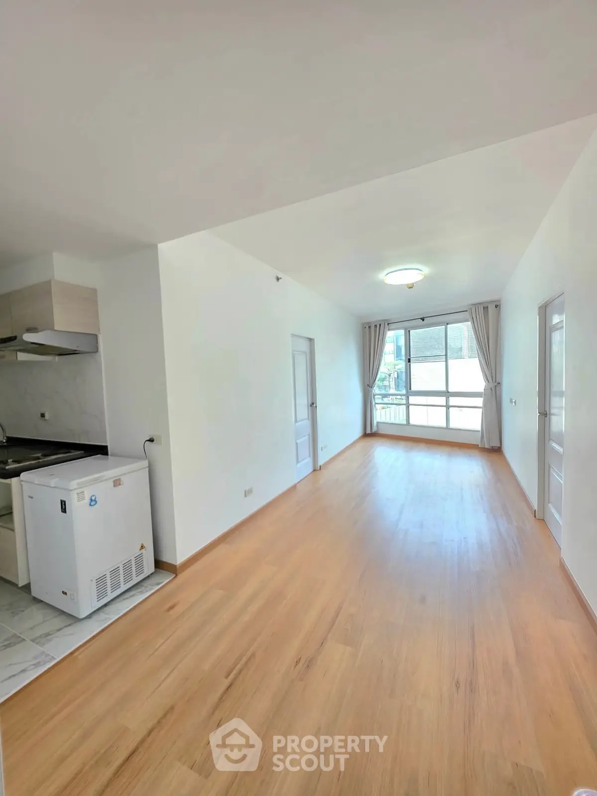 Bright and spacious apartment with open layout and wooden flooring, featuring a compact kitchen area.