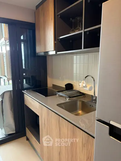 Modern kitchen with sleek wooden cabinets and compact design, featuring a glass door leading to a balcony.