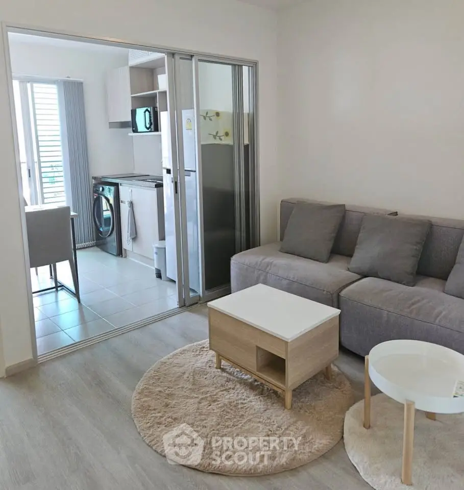 Modern living room with cozy sofa and open kitchen layout, featuring sleek appliances and stylish decor.