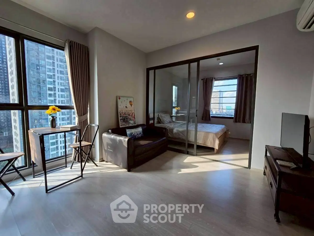 Modern apartment with glass-walled bedroom and city view, featuring sleek furniture and natural light.